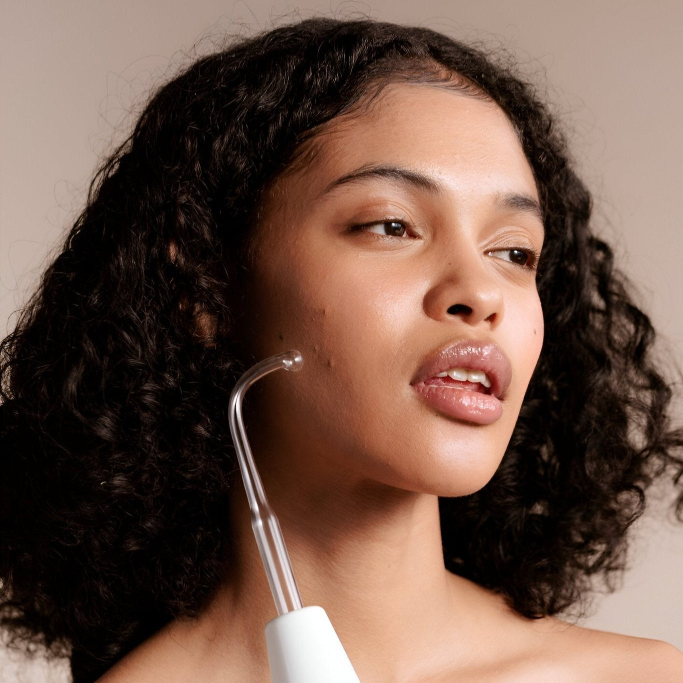 Woman using a white electronic device on her face against a neutral background