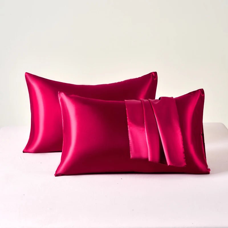 Three pink satin pillows on a white surface with a light gray background