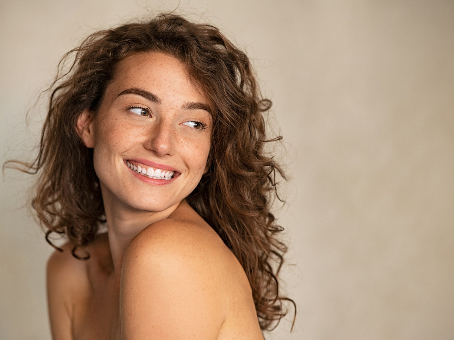 Woman with curly hair smiling against a plain background