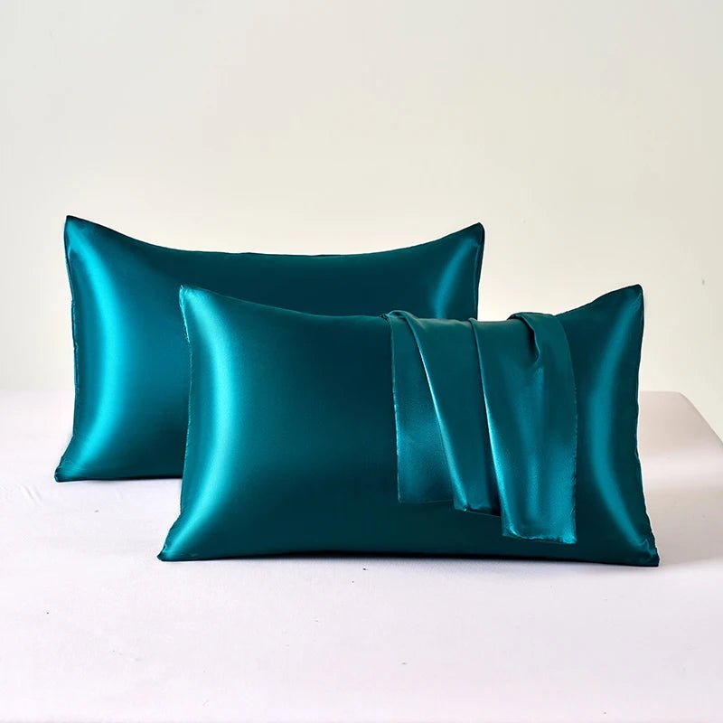Two teal satin pillowcases on a white surface with a light beige background